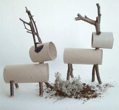 three toilet paper roll sculptures with branches sticking out of them and dirt on the ground