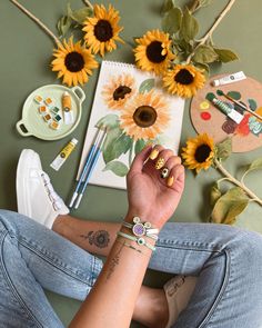 a woman sitting on the floor with sunflowers and other art supplies around her