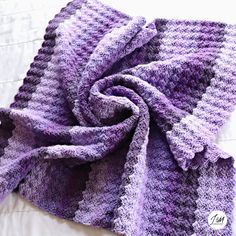 a purple and white knitted blanket laying on top of a bed next to pillows