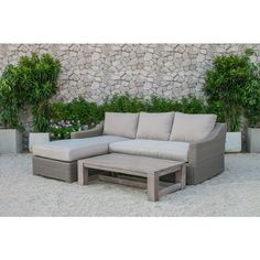 a couch and coffee table sitting in front of a stone wall with potted plants