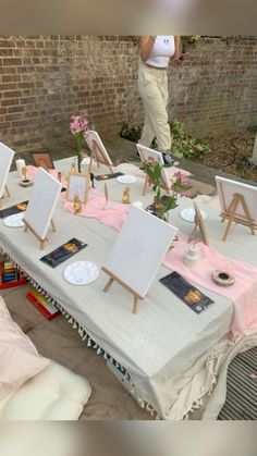 a table with several easels and paintings on it, in front of a brick wall