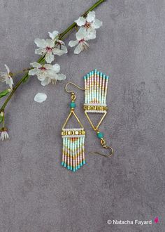 two pairs of earrings sitting on top of a table next to some white and pink flowers