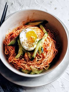 a white bowl filled with noodles and an egg on top of it next to chopsticks