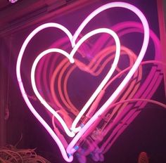 a heart shaped neon sign hanging from the side of a building