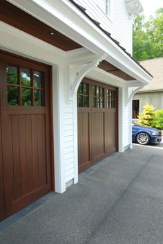 two brown garage doors in front of a white house with a blue car parked on the driveway