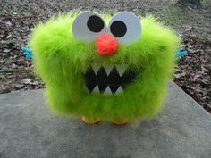 a green stuffed animal with big eyes and mouth on top of a rock in the woods