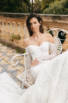 a beautiful woman sitting on top of a white bench wearing a wedding dress with long sleeves