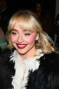 a woman with blonde hair wearing a black and white fur coat smiling at the camera