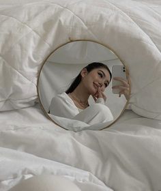 a woman laying in bed looking at her cell phone and taking a selfie with the mirror