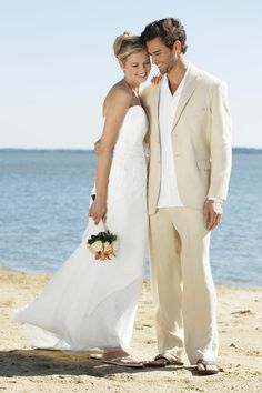 a bride and groom standing on the beach