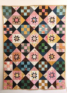 a quilt hanging on the wall with many different colors and shapes in it's center