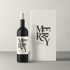 a bottle of red wine next to a white box on a gray surface with the word merry written in black