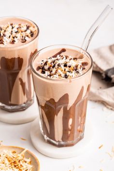 two glasses filled with ice cream and chocolate on top of a white table next to a spoon