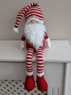 a red and white knitted santa claus doll sitting on a table with his legs crossed