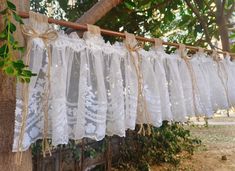 several white laces hanging from a wooden pole in front of trees and greenery