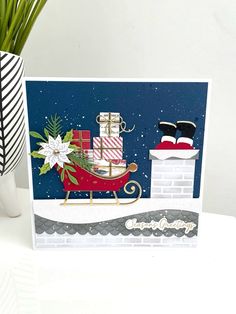 a christmas card with a santa sleigh and gifts on it, sitting next to a potted plant