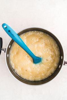 a blue spatula is in a saucepan on the stove top with some food