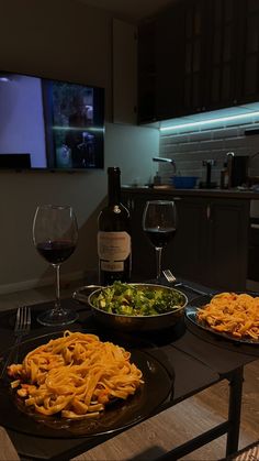 two plates of food on a table with wine glasses and a television in the background