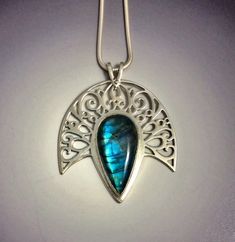 "The deep blue flash on this Labradorite was so glorious that it needed a halo. Enter a sheet of sterling silver and a jeweller's saw and we made the halo a reality. This gem's setting has been handcrafted with meticulous care - each tiny cutout is accomplished with precision and all corners and edges have been filed and polished until they shine with glory!  The pendant measures 41 X 45mm (approximately 1 3/4\" X 1 3/4\"). The chain is a snake style Italian Silver and measures 18\"." Celestial Silver Labradorite Jewelry, Hand Forged Labradorite Blue Jewelry, Hand Forged Blue Labradorite Jewelry, Celestial Teardrop Sterling Silver Jewelry, Celestial Sapphire Sterling Silver Jewelry, Celestial Style Sapphire Jewelry In Sterling Silver, Handmade Celestial Sapphire Jewelry, Unique Sapphire Sterling Silver Jewelry, Silver Teardrop Celestial Jewelry