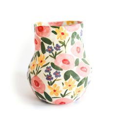 a flowered vase is sitting on a white surface with pink, yellow and blue flowers