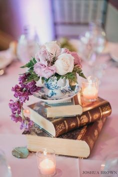 a table topped with books and flowers on top of each other next to a candle