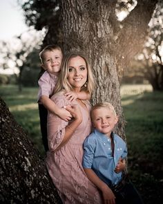 a woman and two boys are posing for a family photo in front of a tree