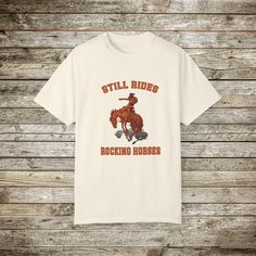 Check out my funny new wild west rodeo cowboy graphic T-Shirt, Done in the Retro Style of the 80s and 90's, this graphic western shirt, pokes gentle fun at the manly and bravery it takes to ride a bucking bronc horse. Every now and then you have to step back and say wow! Look at that guy ride! and wonder... How many rocking horse the went through as a toddler... ☺️??? Gotta love a cowboy! This super comfy comfort color tee has a relaxed fit and the cotton is soft and durable. This will make a great gift for the guy with a sense of humor! Comfort Colors Tshirts: About the Designer of FlooredByArt Studios: ☀️As an artist I try to capture the beauty of nature and the spirit of beloved animals with these stunning archival quality prints. Each design is crafted using cutting-edge digital artist Western Style Relaxed Fit Graphic T-shirt, Western Style Relaxed Fit T-shirt With Graphic Print, Western Style Crew Neck T-shirt With Graphic Print, Western Style Relaxed Fit T-shirt With Screen Print, Short Sleeve T-shirt With Letter Print For Western-themed Events, Western Style Cotton Graphic T-shirt, Western Style Cotton T-shirt With Graphic Print, Western Style Screen Print T-shirt For Western-themed Events, Retro Rodeo Crew Neck T-shirt