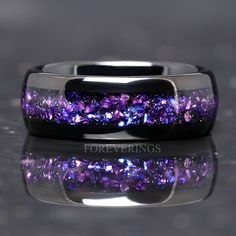 a ring with purple and blue glitters on the inside is sitting on a reflective surface