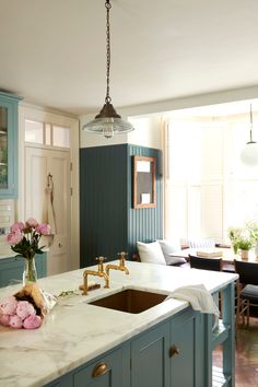 a kitchen with blue cabinets and marble counter tops, an island sink and hanging lights