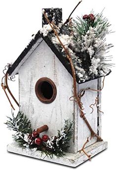 a white birdhouse decorated with pine cones, berries and evergreens is shown in front of a white background