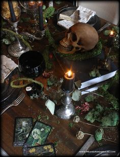 a table topped with candles and skulls on top of it's wooden table covered in greenery