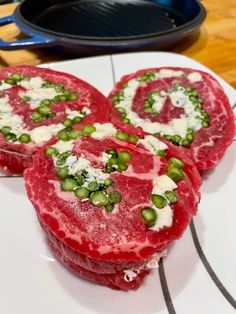 three pieces of raw meat on a white plate with green peas and cream cheese in the middle