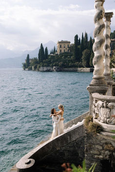 two women standing on the edge of a pier next to water