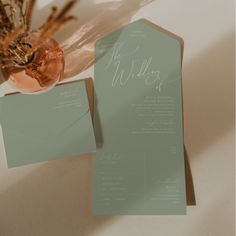 the wedding stationery is set on top of an envelope and some dried flowers in a vase