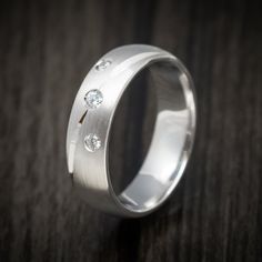 a wedding ring with three diamonds on it sitting on a wooden table in front of a dark background