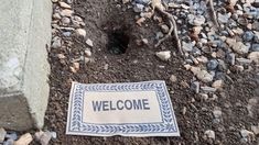 a welcome sign laying on the ground next to some rocks and gravel with a hole in it