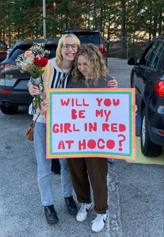 two women standing next to each other holding a sign that says will you be my girl in red at hoo?