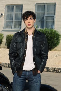 a young man standing in front of a motorcycle wearing a leather jacket and white t - shirt