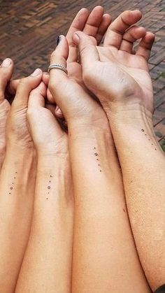 four people are holding their hands together with small dots on the wrist and hand tattoos