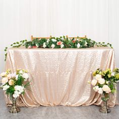 two vases filled with flowers sitting next to a table covered in a gold cloth