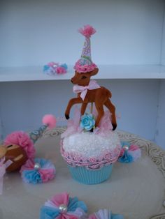 there is a cupcake with a deer on it and pink flowers around the cake