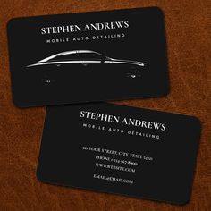 two black business cards sitting on top of a wooden table with a car logo in the middle