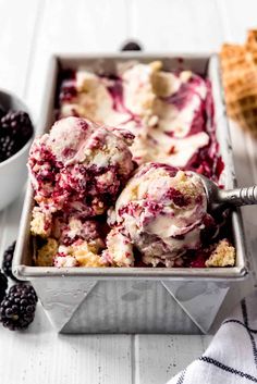 two scoops of ice cream in a metal pan with berries and waffle cones