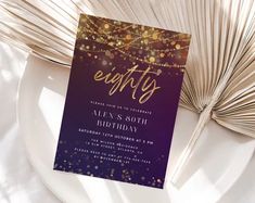 a purple and gold birthday party card sitting on top of a white plate next to an open book