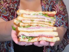 a person holding a sandwich in their hands with meat, cheese and vegetables on it