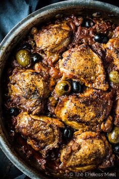 a pan filled with chicken and olives on top of a table