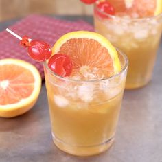 two glasses filled with oranges and cherries sitting on a table next to an orange slice