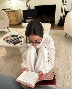 a woman sitting on the floor reading a book in front of a fire place and fireplace