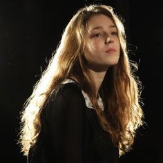 a woman with long hair standing in front of a black background and looking off to the side