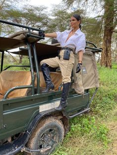 a woman standing on the back of a green truck with an open top and luggage strapped to it